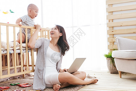 儿子婴儿期女人年轻妈妈在家边看孩子边使用电脑图片