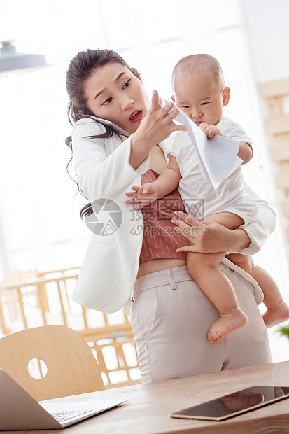 不看镜头爱户内年轻妈妈抱着孩子在家办公图片