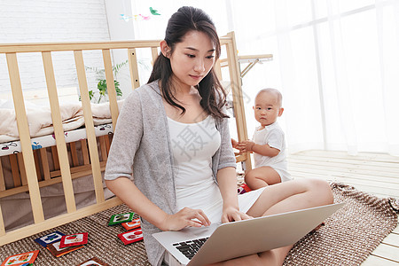 快乐母子幼儿年轻妈妈在家边看孩子边使用电脑图片
