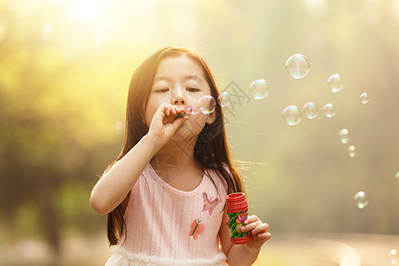 泡泡小孩可爱的女孩在户外吹泡泡背景