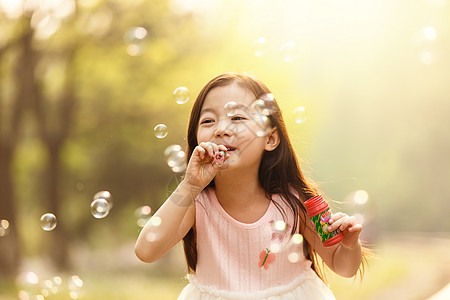 小孩嬉戏可爱的女孩在户外吹泡泡背景