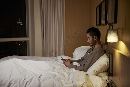 夜晚坐在床上看手机的成熟男性图片