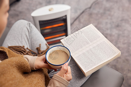 取暖器旁看书喝咖啡特写图片
