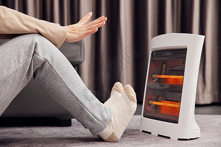 冬天美女使用取暖器温暖手脚特写背景