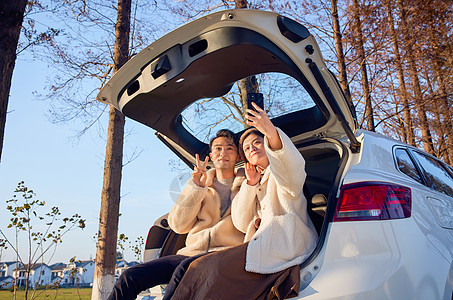 年轻情侣自驾出游坐在汽车后备箱拍照图片