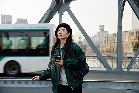 手捧咖啡站在桥上看风景的青年女性背景图片