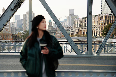 手捧咖啡站在桥上看风景的青年女性背景图片
