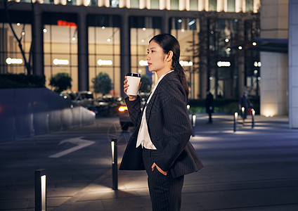 夜晚站在办公楼前喝咖啡的商务女性图片