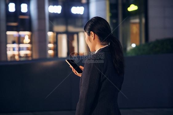 深夜站在写字楼外使用手机的女性背影图片