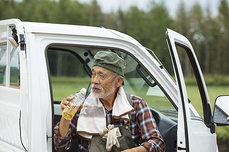 老人靠着农用车休息喝水背景图片