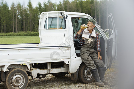 农民靠着农用车休息喝水背景图片