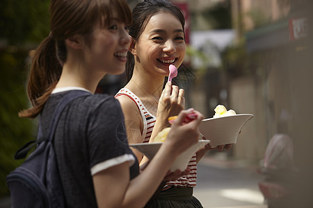 吃芒果的女孩两个女游客在街上拿着刨冰边走边吃背景