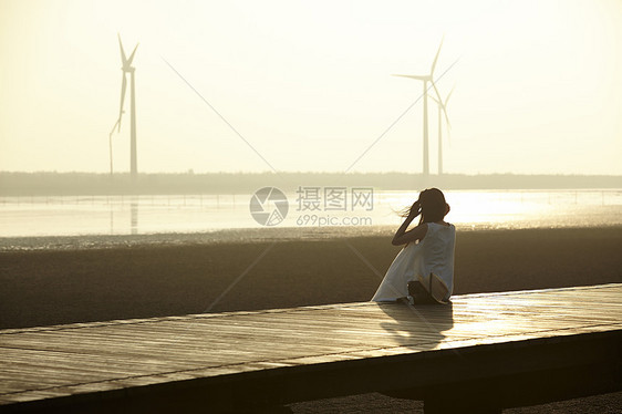 日落时女人坐在在湿地栈道的剪影图片