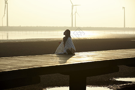 日落时女人坐在湿地栈道的剪影图片