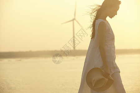 日落时女人在湿地拿着帽子的剪影图片