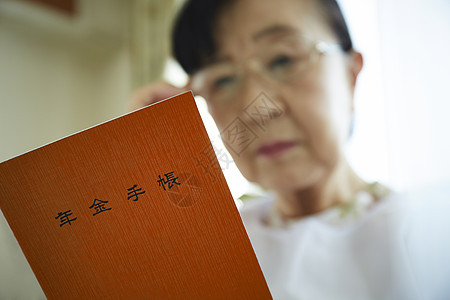 独居老妇人戴着眼镜看年金手账本背景图片