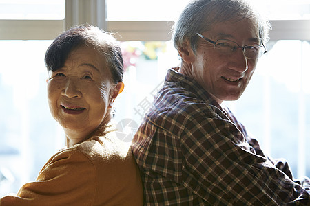起居室茶桌旁背靠背坐着的老年夫妻笑着看镜头图片