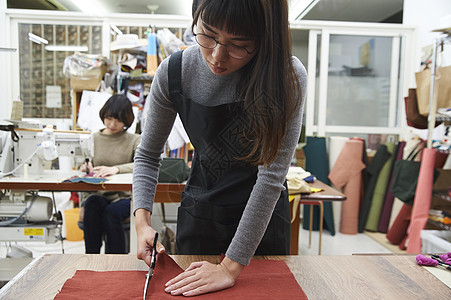 剪布料在制作手提包的女缝纫工背景