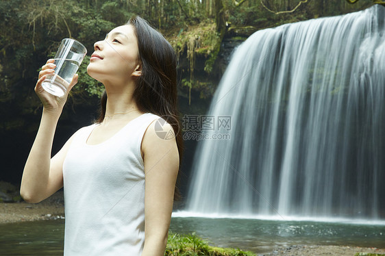 站在小溪边享受瀑布的女人在喝水图片