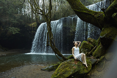 年轻女性坐在小溪旁的岩石上图片