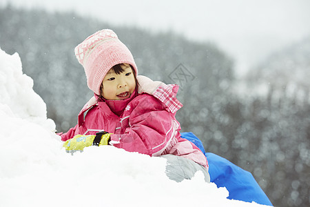 玩雪球小女孩趴在积雪上玩耍的小女孩背景