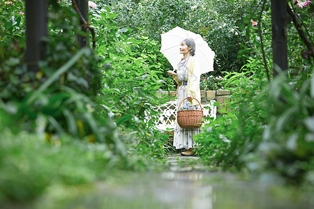 拿着遮阳伞站在庭院里的老妇人图片