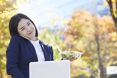 拿着沙拉歪头夹住手机打电话的女青年图片