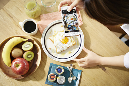 用手机拍摄自制早餐的职业女性图片