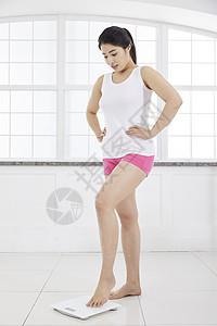 年轻女子小心的站在体重秤上图片