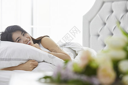床上抱着枕头微笑的青年女子植物高清图片素材
