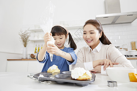 母亲微笑的看着女儿挤奶油做甜品图片