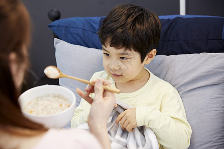 妈妈照顾生病在床的男孩吃粥背景图片