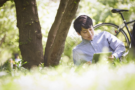 坐在草坪上看平板电脑的青年男子图片