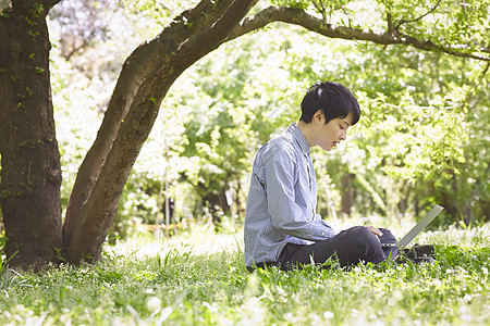 公园里低头使用笔记本电脑的男青年图片