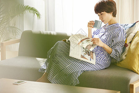 沙发上喝着咖啡看杂志的青年女子图片