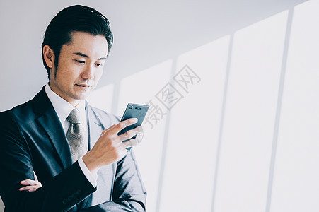 处理黑发法人站立对白色墙壁的上司男当看手机时图片