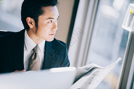 男白领处长依赖读一张报纸的上司人当朝向在窗口的一个位子的个人计算机时图片