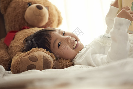 室内抱玩具熊的女孩在床上图片