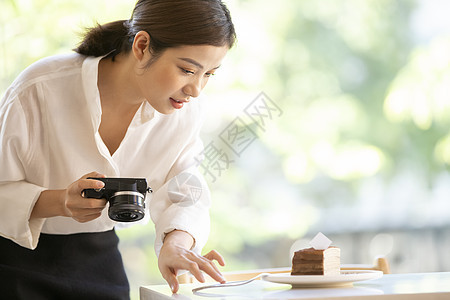 拿着相机拍甜品照片的年轻女子图片