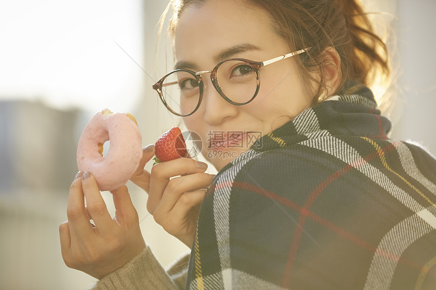 拿着甜甜圈和草莓微笑的年轻女子图片