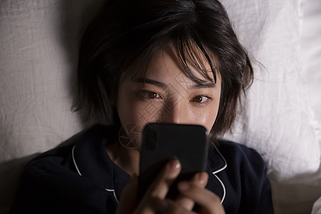 躺在床上玩手机的年轻女子图片