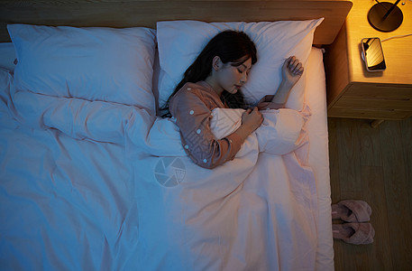 手机充电俯拍夜晚开着灯睡觉的年轻女性背景
