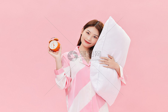 身着睡衣的年轻少女手拿闹钟和枕头图片