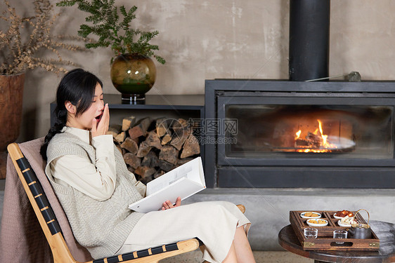 坐在火炉边看书的女性犯困图片