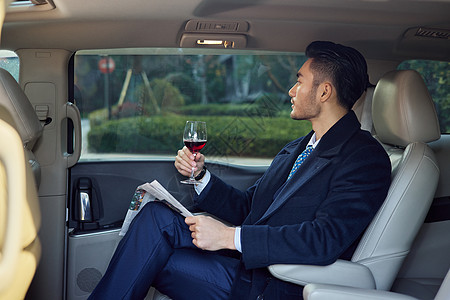 商务男性在车内看报纸喝红酒图片