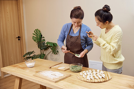 妈妈和女儿做饭女儿给包饺子的母亲拍照背景