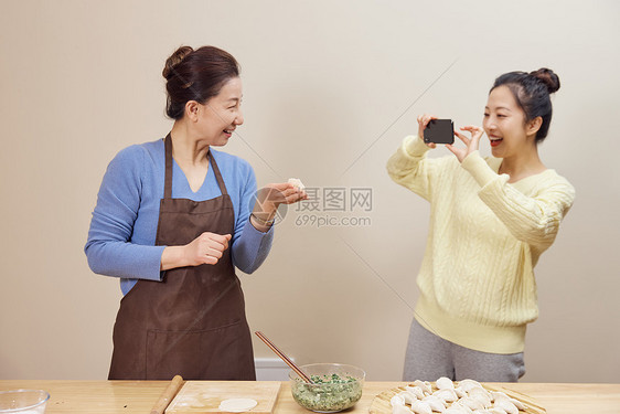 女儿给包饺子的母亲拍照图片