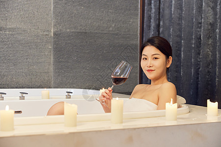 年轻美女浴缸泡澡喝红酒背景图片
