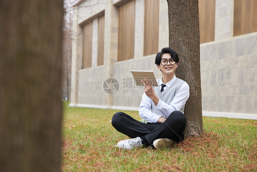 青年男性学生坐草地上学习图片