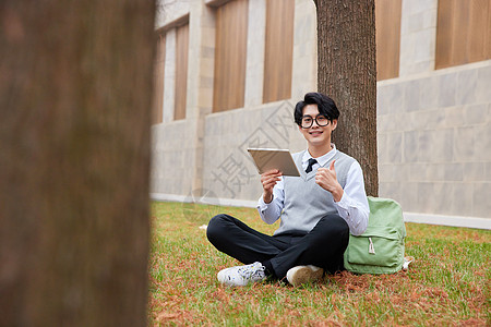 青年男性学生坐草地上看平板电脑背景